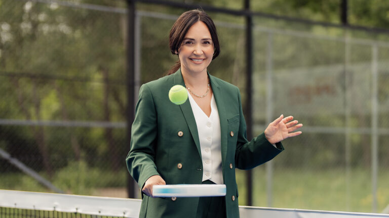 Eine Frau in Business-Kleidung mit einem Padelschläger und -ball.